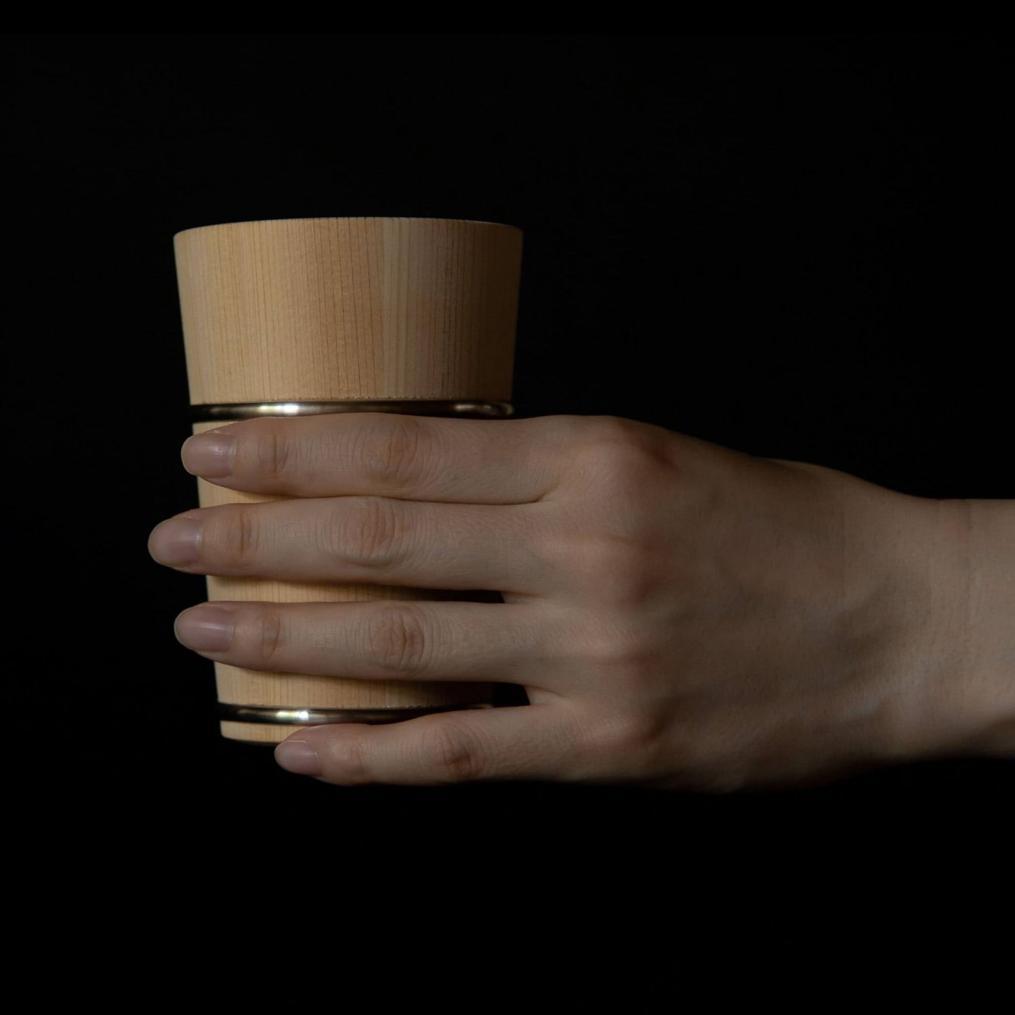 Hand holding wooden Hinoki cup with metal bands