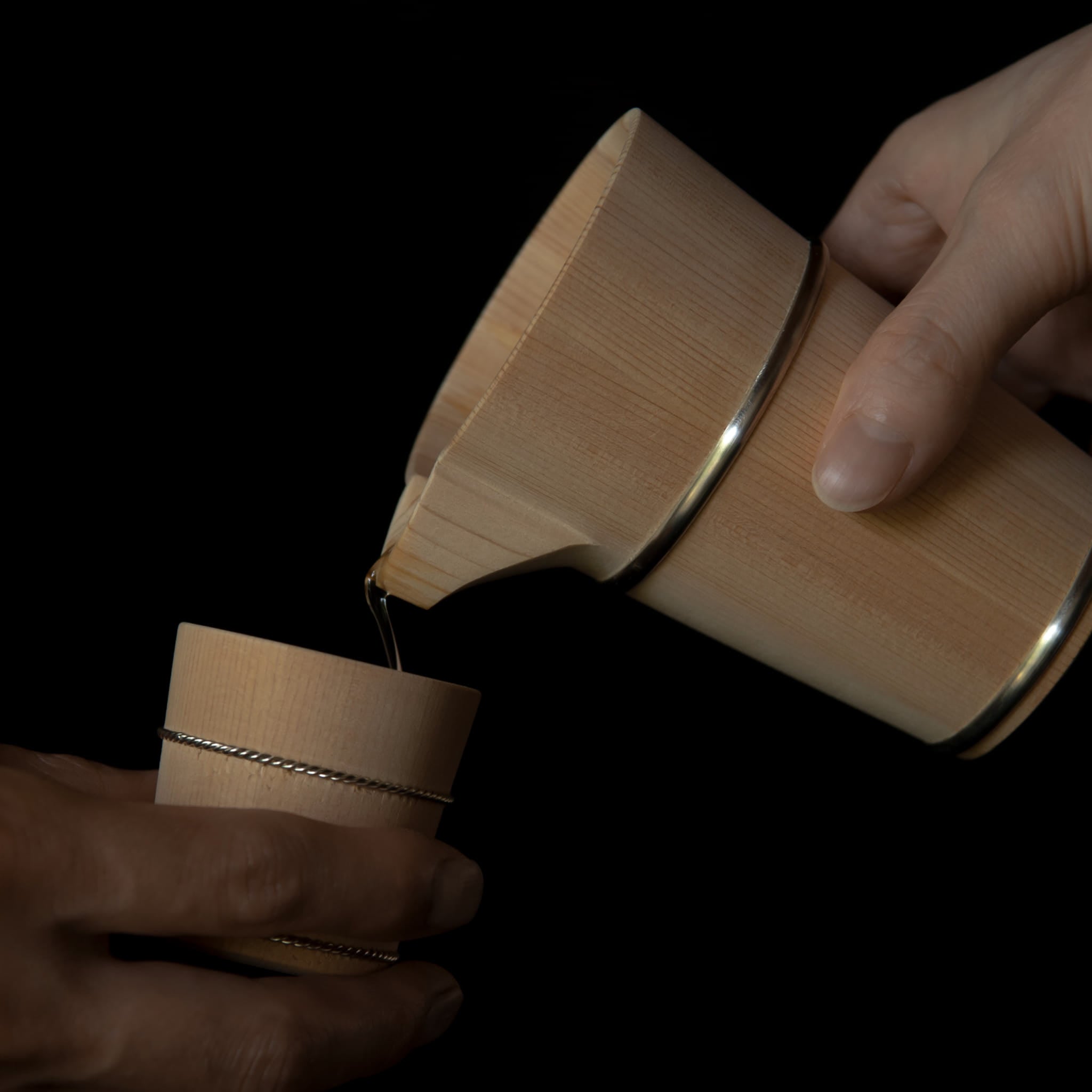 Wooden Hinoki sake carafe pouring sake into a wooden Hinoki sake cup